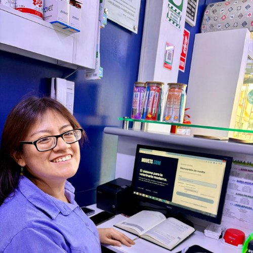 Una trabajadora de una clínica veterinaria sonríe en recepción, con muvets abierto en la pantalla.
